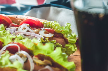 two fresh hot dogs on a wooden Board, glasses with Cola and American flag