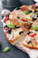 pizza with tomatoes, mushrooms, olives and peppers served on a wooden table