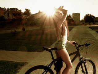 Fototapeta premium Young attractive woman is sitting on bicycle outdoors at sunset time. Retro styled background soft focus instagram color filter