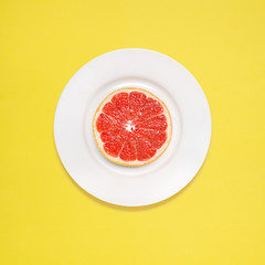 Grapefruit for breakfast / Red grapefruit slice on white plate on yellow background.