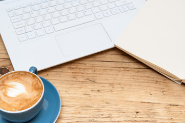 Fresh cup of coffee and laptop computer on a wooden table backgr