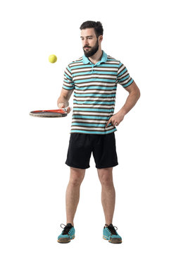 Relaxing tennis player in polo shirt bouncing ball with racket. Full body length portrait isolated over white studio background.