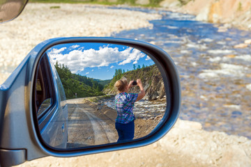 Rear view mirror. A woman photographs the landscape on a smartphone. 