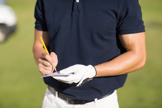 Midsection of golfer writing on score card 