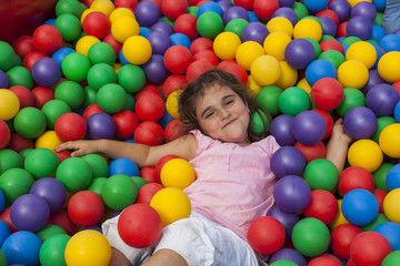 Fototapeta na wymiar Girl lie down in a colorful plastic ball pool