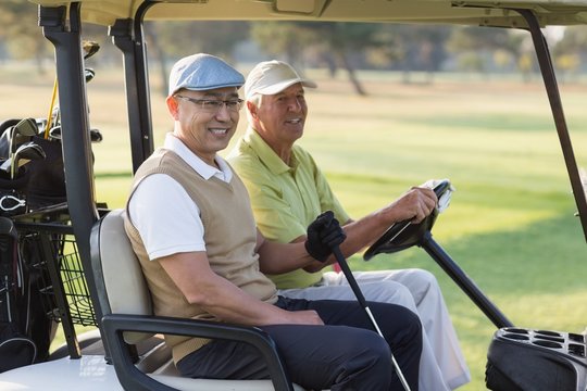 Smiling male golfer friends sitting in golf buggy 
