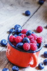 Fresh raspberries and blueberries in red enamel mug, vintage woo