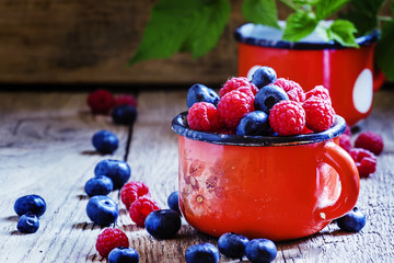Fresh raspberries and blueberries in red enamel mug, vintage woo