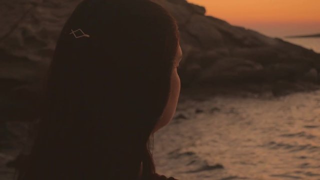 A lowkey shot of a young lady contemplating the sea during sunset
