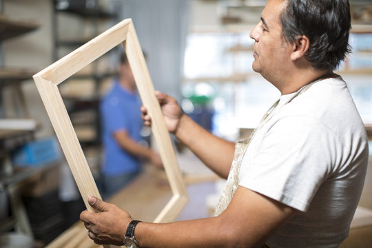 Man looking at wooden frame for canvas preparation in workshop