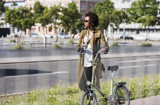 Young woman with smartphone and earphones pushing bicycle