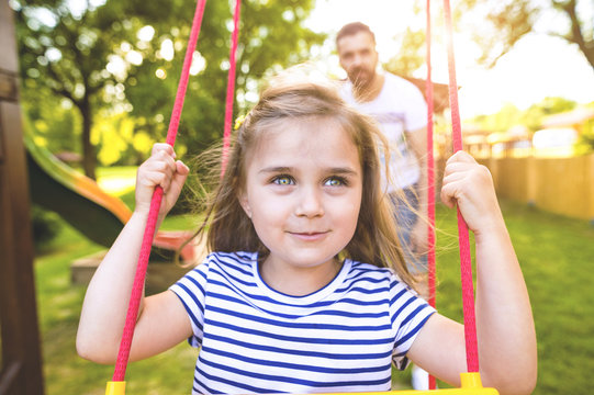 Portrait of happy little girl on a swing with father in the background