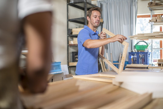 Man looking at wooden frame for canvas preparation in workshop