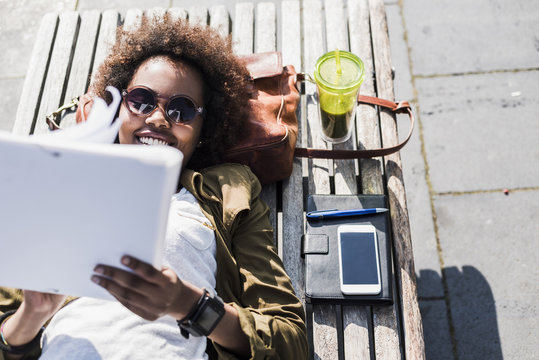 Portrait of smiling woman lying on a bench reading notes