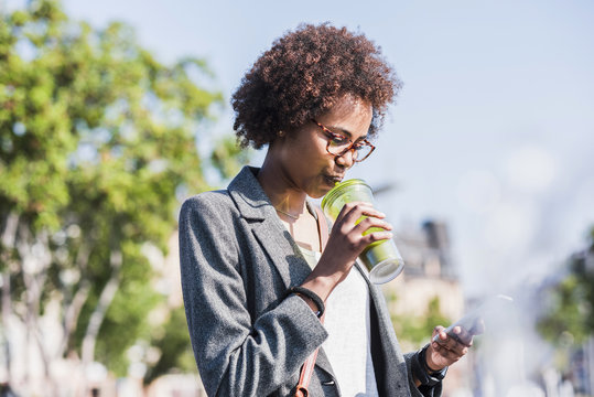 Woman drinking beverage while looking at her smartphone