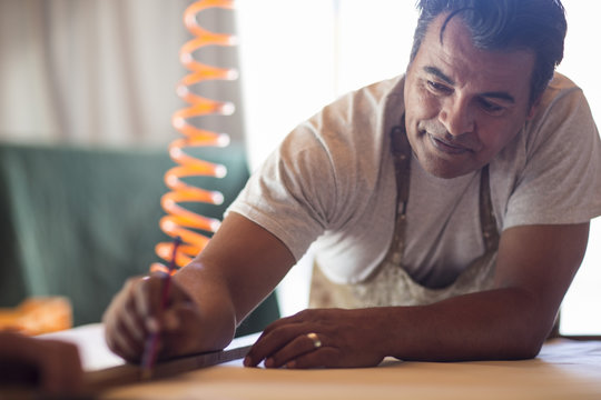 Man in canvas workshop marking piece of wood with pencil