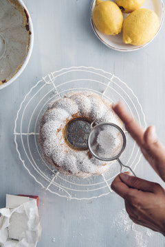 Woman's hands sprinkling icing sugar on ring cake