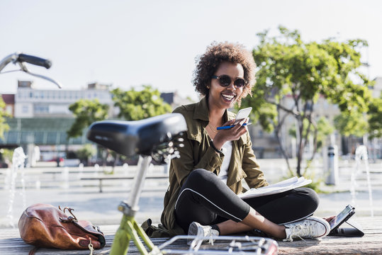 Portrait of young woman sitting on a  bench using smartphone and digital tablet