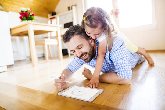 Father and daughter lying on floor, drawing on digital tablet