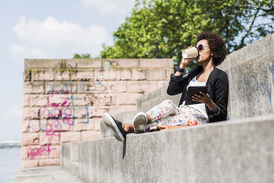 Young businesswoman with digital tablet drinking coffee to go at riverside