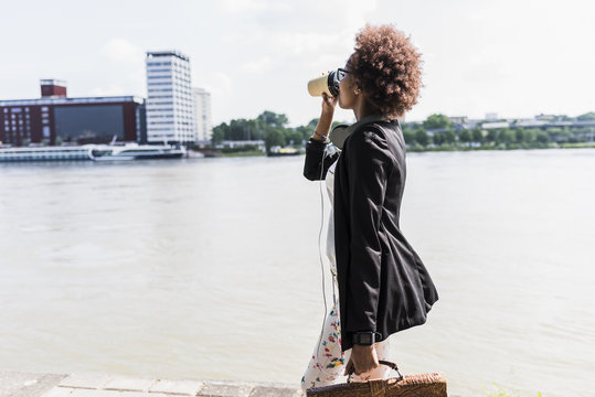 Germany, Mannheim, young businesswoman drinking coffee to go while walking at riverside