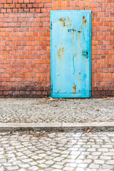 Rusty but colorful old door in brick wall upon cobblestone
