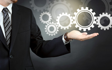 Geschäftsmann in Business Anzug hält Zahnräder als Symbolbild für Kooperation und Teamwork