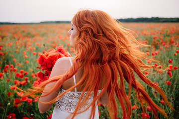 Beautiful young red-haired woman in poppy field with flying hair