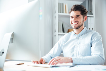 Smiling young businessman using laptop computer in office