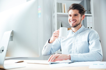 Fototapeta premium Young businessman in casual cloth drinking coffee in office