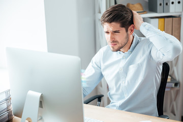 Pensive businessman sitting at the table with laptop in office