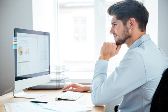 Side view of businessman sitting using personal computer in office