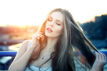 Outdoor portrait of young pretty sexy woman with sensual lips posing at roof at the end of bright sunset. Lovely soft back light.