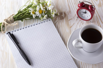 blank notebook, alarm clock, charmomile and coffee cup.