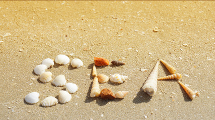 Fototapeta na wymiar SEA word made of seashells on the sandy beach, Thailand. (warming color tone)