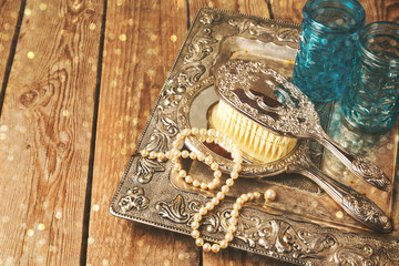Vintage hand mirror and hairbrush on silver tray over wooden background