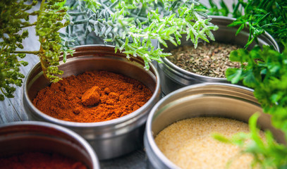 Spices in metal containers and fresh herbs on wooden table