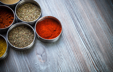 Spices and herbs in metal containers on wooden table