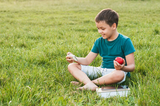 Young boy with a phone and apple on the grass