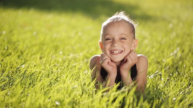 Little girl at sunset on the grass and smiling at camera