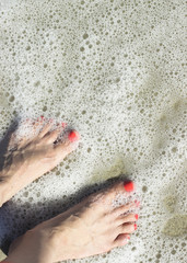 Bare female feet on the shore washed by the sea