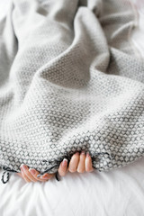 Woman hiding from the problems under the gray blanket. Photo of bed with gray blanket and two...
