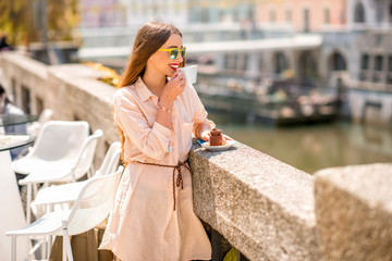 Young woman enjoying coffee with chocolate cake near the river in the center of Ljubljana city....