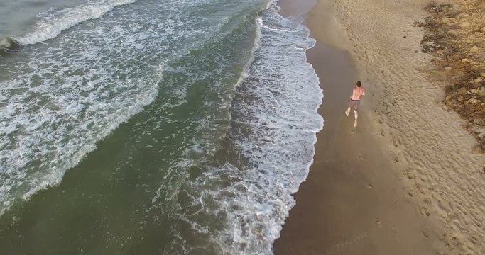 Morning jogging guy along the surf line of the sea beach in summer