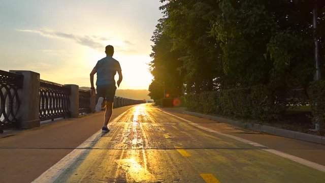 Man in blue uniform running on summer sunset embankment along bicycle road, Moscow. Super slow motion steadicam shot at 240 fps