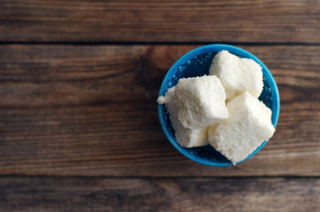 Rahat lakoum pieces in coconut flakes in a blue small plateau on a wooden table. East sweets, Turkish delight 