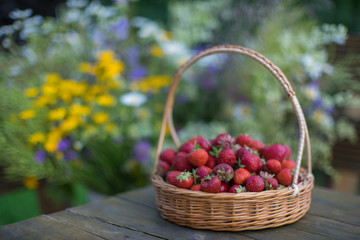 Strawberries in a wicker basket on a background of summer bouque