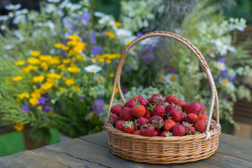 Strawberries in a wicker basket on a background of summer bouque