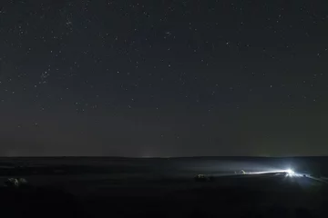 Papier Peint photo Nuit Ciel nocturne d& 39 été au-dessus de la plaine. Une seule voiture éloignée s& 39 allume la nuit dans un pré avec un ciel étoilé clair.