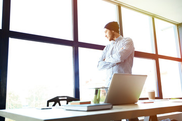 Pensive young handsome man working on laptop while sitting at his working place